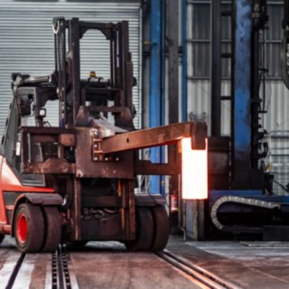 Das Gerät hat ein spezielles Anbaugerät für den Transport zum nächsten Bearbeitungsschritt. Das Gerät transportiert ein glühendes Eisen über das Gelände.