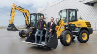 Dominik Haag und Markus Köhler von Yanmar Compact Equipment Europe stehen in der Schaufel eines Fahrzeugs.
